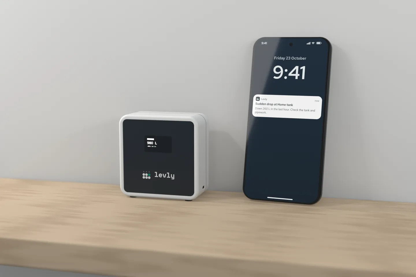 The Levly hub on a shelf showing 980 L, beside a phone lock screen with a Levly alert: Sudden drop at Home tank, down 260 L in the last hour, check the tank and pipework