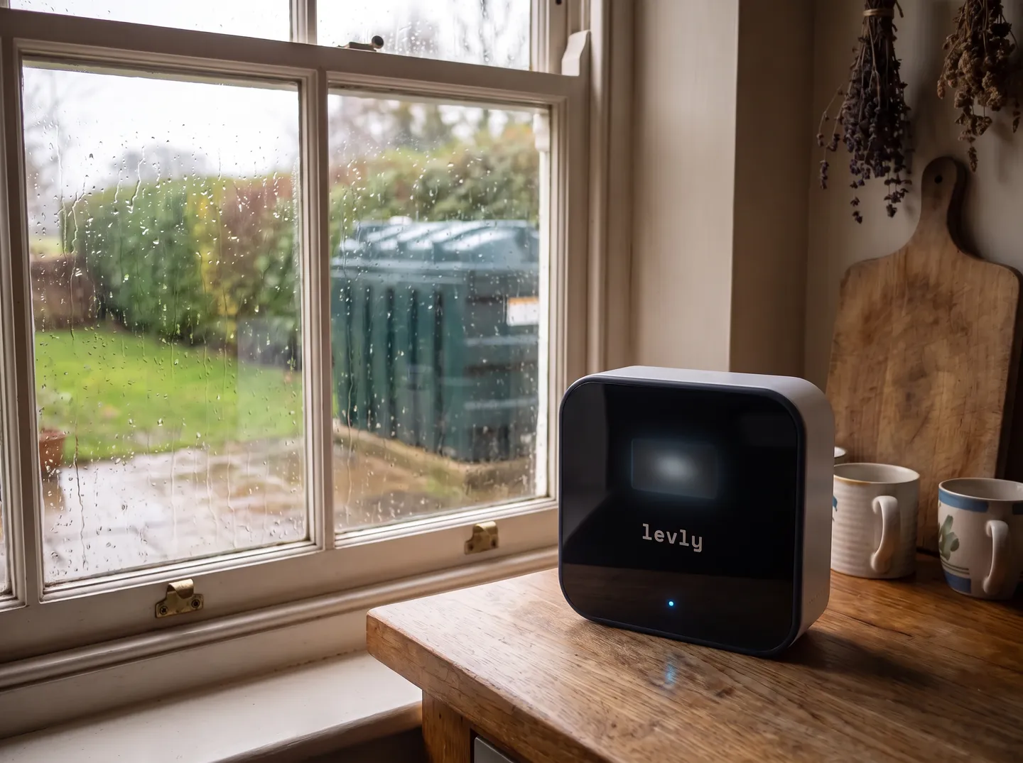 A Levly hub on a kitchen worktop, with a green heating-oil tank in the rain outside the window