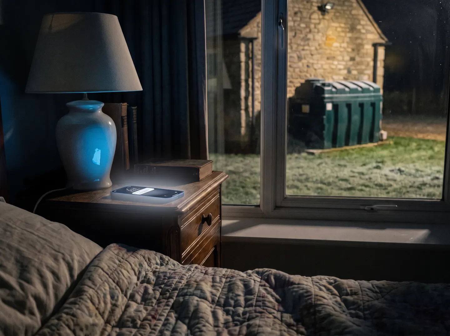 A phone lighting up on a bedside table at night, with the oil tank outside the window